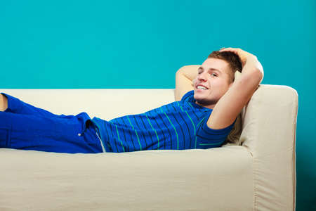 Young man relaxing on couch, teen positive boy laying lazy on bed blue backgroundの写真素材