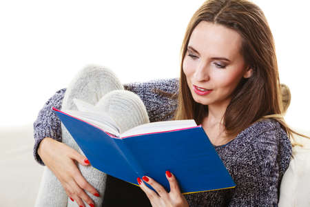 Leisure, education, literature and home concept. Woman sitting on couch reading book at home