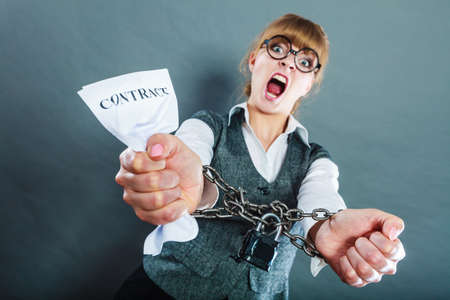 Business and stress concept. Furious businesswoman in glasses with chained hands holding contract grunge backgroundの写真素材