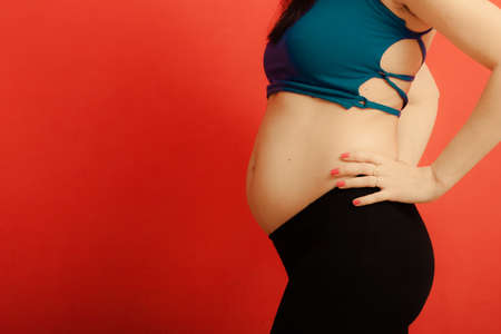 New life concept. Pregnancy, motherhood and happiness. Closeup tummy of pregnant woman on redの写真素材