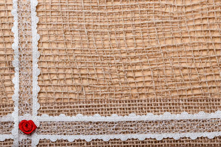 valentines day, wedding, invitation or greeting card. red decorative silk rose flowers, lace ribbon on rustic burlap cloth . border frame.の写真素材