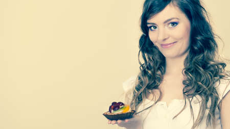 Bakery, sweet food and people concept. smiling cute woman curly hair holding fruit cake cupcake in...