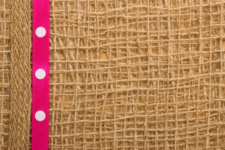 Polka dotted pink ribbon on brown mesh material, natural burlap の写真素材