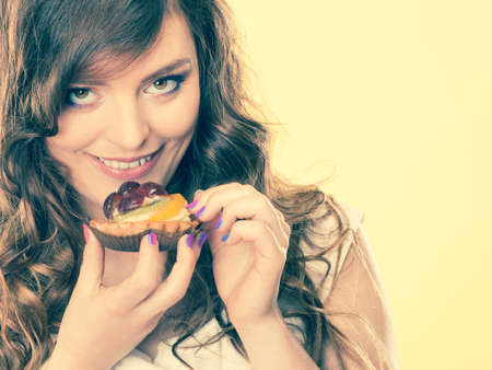Bakery, sweet food and people concept. smiling cute woman curly hair holding fruit cake cupcake in...