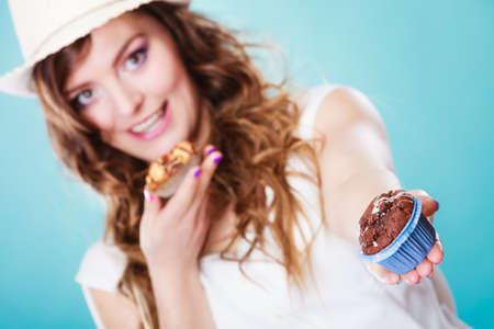 Bakery, sweet food and people concept. Closeup smiling summer woman curly hair straw hat holding cakes cupcakes in hands blue backgroundの写真素材