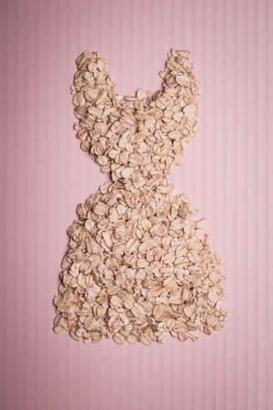 Dieting healthy eating slim down concept. Female dress shape made from oatmeal thin figure on pinkの写真素材