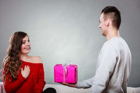 Couple and holiday concept. Handsome man surprising cheerful woman with gift boxの写真素材