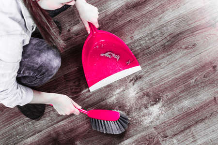 Cleanup housework concept. Closeup cleaning woman sweeping wooden floor with red small whisk broom and dustpan indoorの写真素材