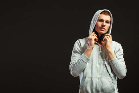 young serious hooded man teen boy with headphones listening to music black の写真素材
