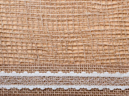 Lace and jute bagging ribbon on brown mesh material, natural burlap backgroundの写真素材