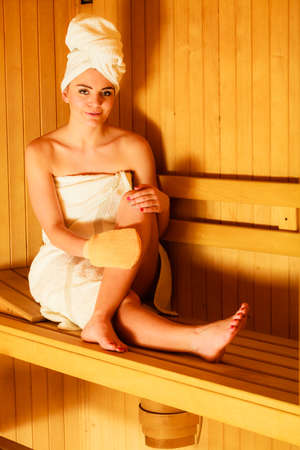Spa beauty treatment and relaxation concept. Woman white towel relaxing in wooden sauna room, making massage with exfoliation gloveの写真素材