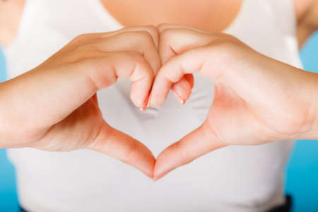 Love, hope and charity concept. Woman hands creating heart sign symbol on blue background. Studio shot.の写真素材