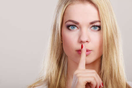 Closeup woman asking for silence or secrecy with finger on lips hush hand gesture. On gray...