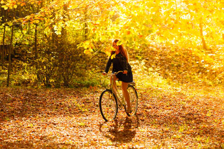 Fall active lifestyle concept,. Beauty young redhaired woman fashion girl relaxing in autumn park with bicycle, outdoorの写真素材