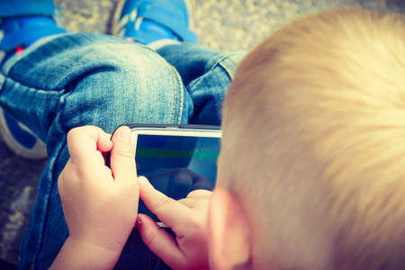 Little boy child kid playing games on smartphone mobile phone outdoor. Technology generation.
