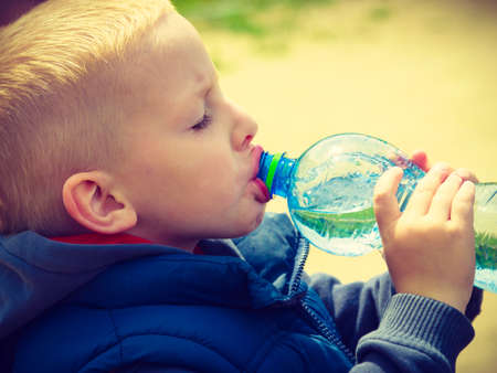 Little thirsty boy child drink water from plastic bottle, outdoorの写真素材
