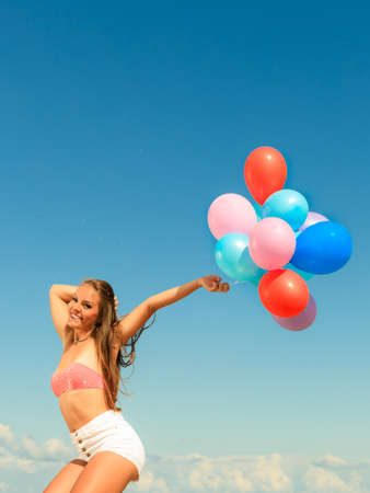 Summer holidays, celebration and lifestyle concept - attractive athletic woman teen girl jumping with colorful balloons outside on beach, sunny dayの写真素材