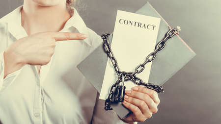 Business concept, limited by contract. Woman holding in hands paper document chained with padlockの写真素材