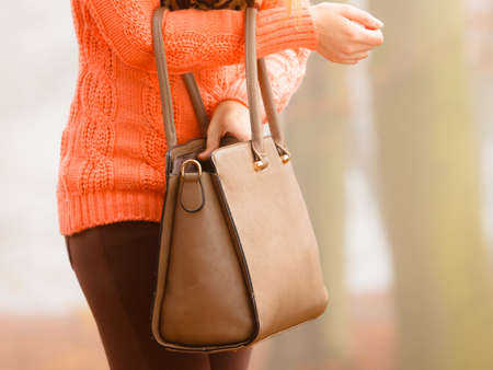 Autumn fashion. Woman fashionable girl wearing vivid clothing holding brown leather bag handbag in hand, walking in autumnal foggy park, outdoorsの写真素材