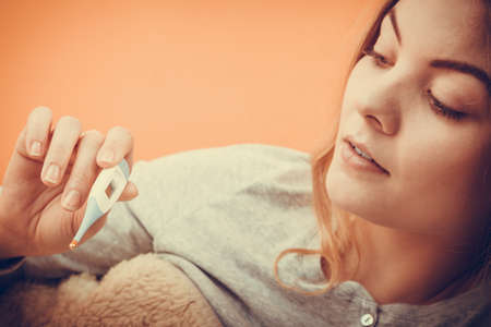Sick ill woman with digital thermometer. Young girl having high fever measuring temperature. Health.の写真素材