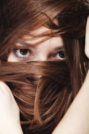 Loneliness stress anxiety and women concept. Closeup portrait beautiful woman dark haired, teen girl covering face by long brown hairs on blackの写真素材