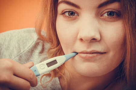 Sick ill woman with digital thermometer in mouth. Young girl having high fever measuring temperature. Health.の写真素材
