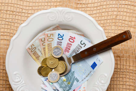 Cost of living, price of food and eating wealth concept. Euro money on kitchen table, plate spoon with coins and banknoteの写真素材