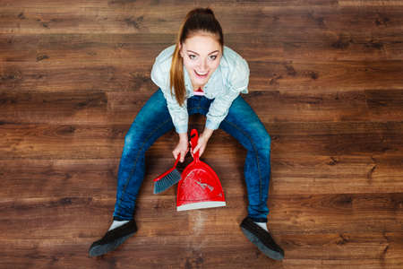 Cleanup housework concept. cleaning woman sweeping wooden floor with red small whisk broom and dustpan unusual high angle viewの写真素材