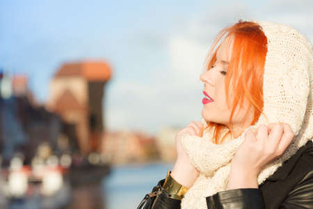 Winter fashion. Beauty girl portrait red hair young woman in warm clothing outdoor enjoying sunlight on sunny day. City Gdansk in the backgroundの写真素材