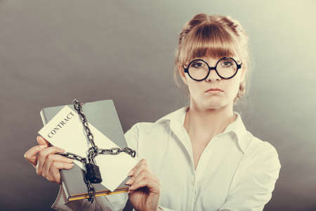 Business concept, limited by contract. Woman holding in hands paper document chained with padlockの写真素材