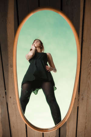 Solitude loneliness concept. Thoughtful young woman looks at the reflection in the mirror outdoors...