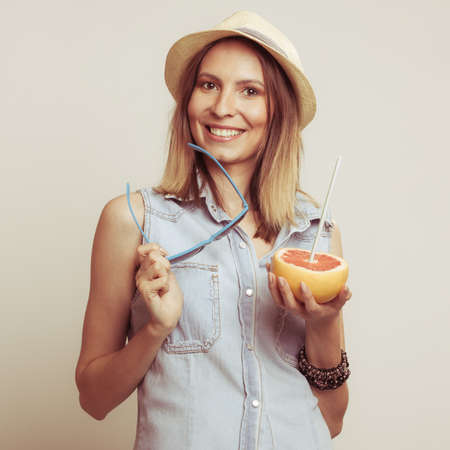Happy glad woman tourist in straw hat holding sunglasses and grapefruit citrus fruit. Healthy diet food. Summer vacation holidays concept.の写真素材