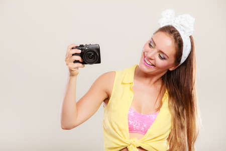 Happy smiling pretty pin up girl with hairband bow taking photo picture with camera. Attractive...