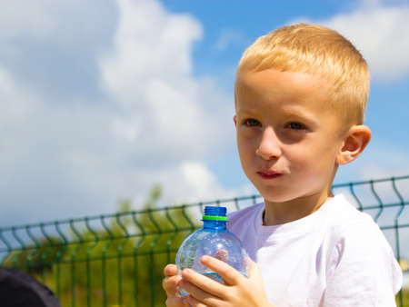 Little thirsty boy child drink water from plastic bottle, outdoorの写真素材
