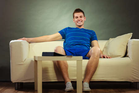 Young man relaxing on couch, tablet and mobile phone laying on tableの写真素材