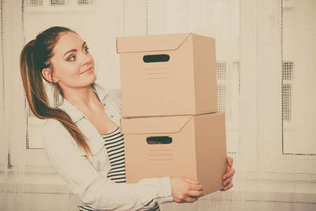 Woman moving in carrying cartons boxes. Young girl arranging interior and unpacking at new apartment house home.  の写真素材