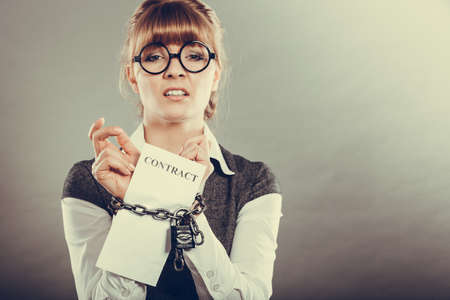 Business concept. Serious businesswoman with chained hands holding contractの写真素材