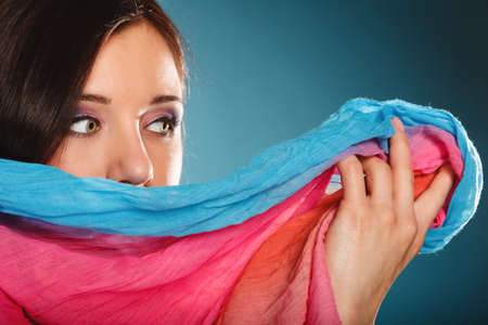 Young woman makeup on eyes hiden her face with multicolored shawl blue backgroundの写真素材