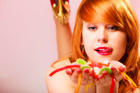 Candy addiction. Multi colored jelly sweets in red haired woman hands. Studio shot.の写真素材