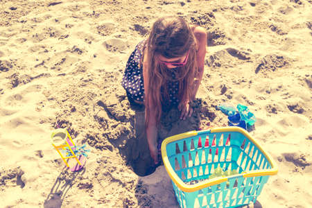 Little girl child with toy having fun on beach. Kid with shovel digging hole in sand. Summer vacation holidays relax.の写真素材