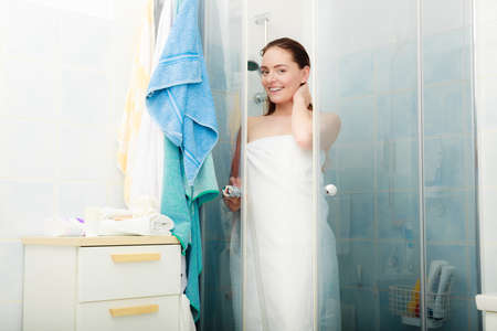 Girl showering in shower cabin cubicle enclosure. Young woman with white towel taking care of...