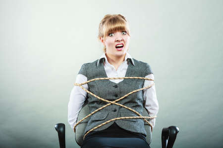 Afraid kidnapped businesswoman tied with rope to chair. Woman kept prisoner. Girl being imprisoned incarcerated.の写真素材