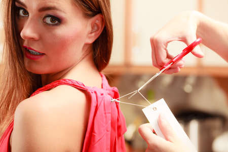 Woman girl removing cutting label board price tag off new dress cloth with scissors. Female after...