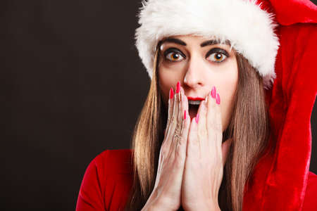 Christmas time. Young woman wearing santa claus hat red dress on black background. Surprised face expression.の写真素材