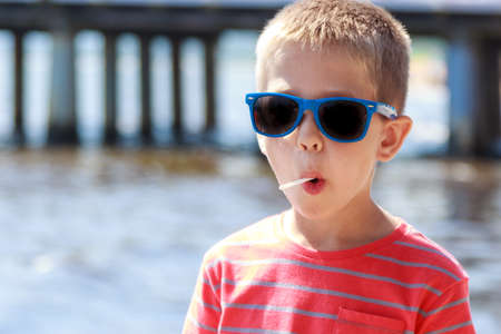 Portrait of little young boy kid child in sunglasses licking lollipop at sea. Summer holidays vacation.の写真素材