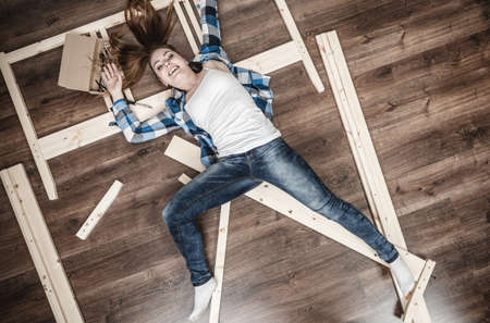 Happy woman having fun assembling furniture at home. Young girl laying in apartment house. DIY.の写真素材