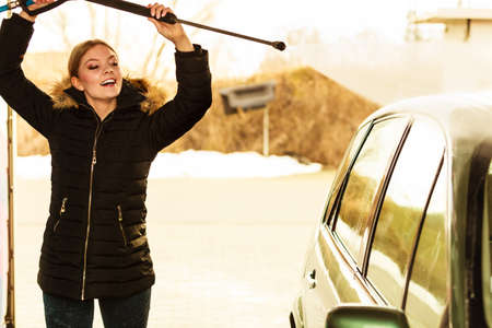 Manual auto wash. Young attractive blonde woman washing the dirty car with foam and pressured water at service station on open airの写真素材