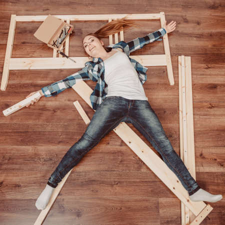 Happy woman having fun assembling furniture at home. Young girl laying on floor arranging apartment house interior. DIY. High angle view.の写真素材