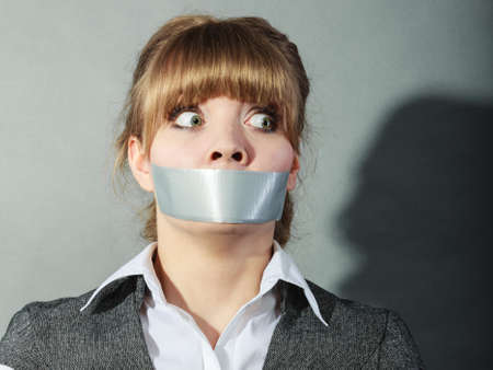 Scared woman with mouth taped shut. Afraid young girl with duct tape on lips. Censorship and freedom of speech concept.の写真素材