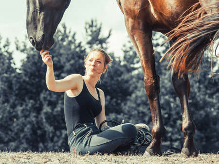 Young woman girl feeding and taking care of brown horse. Female with animal outdoor.の写真素材